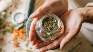 Hands hold a small jar full of dried herbs that make up a natural remedy
